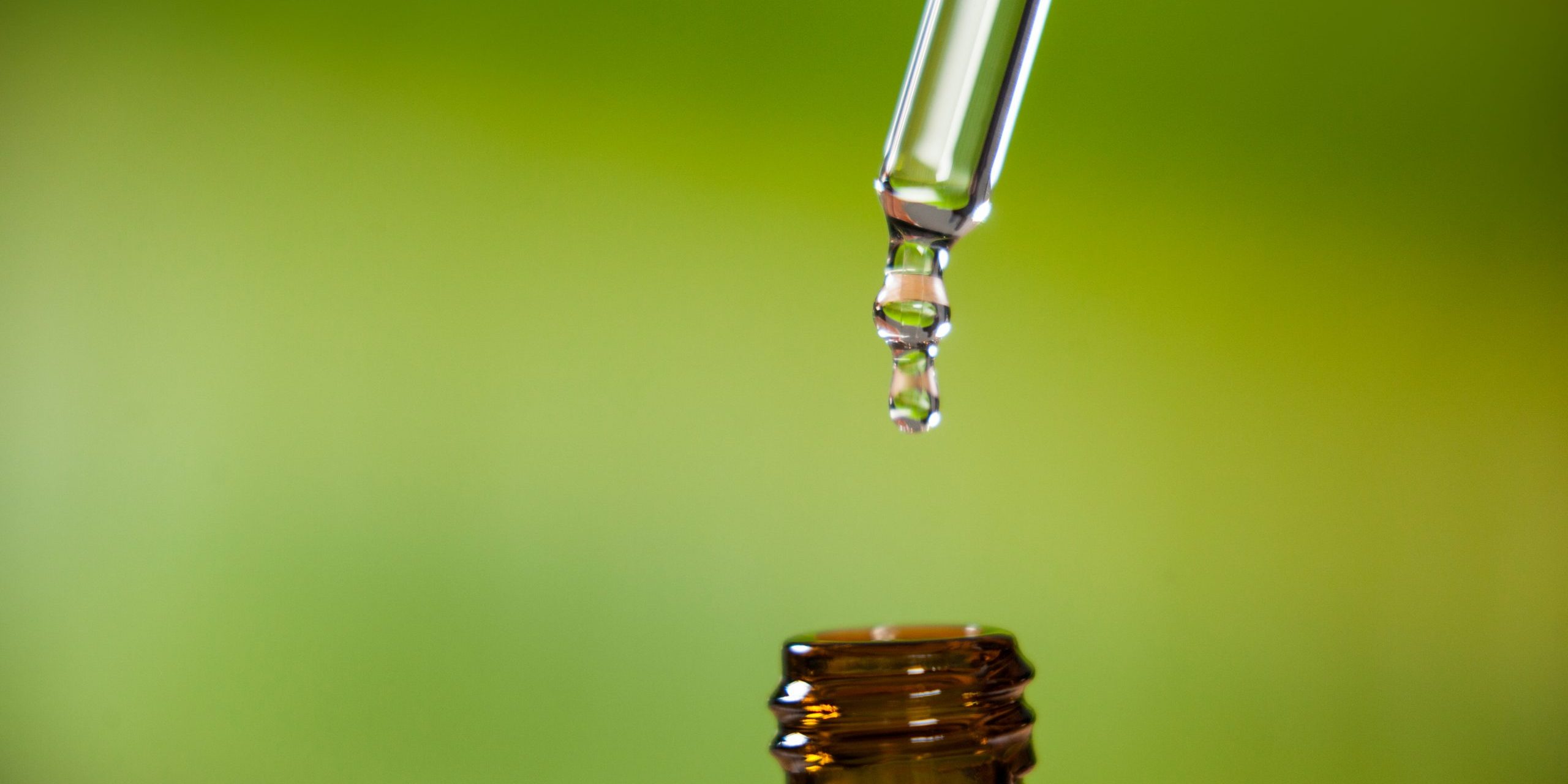 Drop of oil dripping from pipette into bottle of essential oil